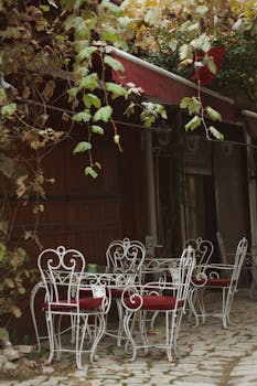 Cozy outdoor café setting with vintage iron chairs and lush foliage, perfect for summer relaxation.