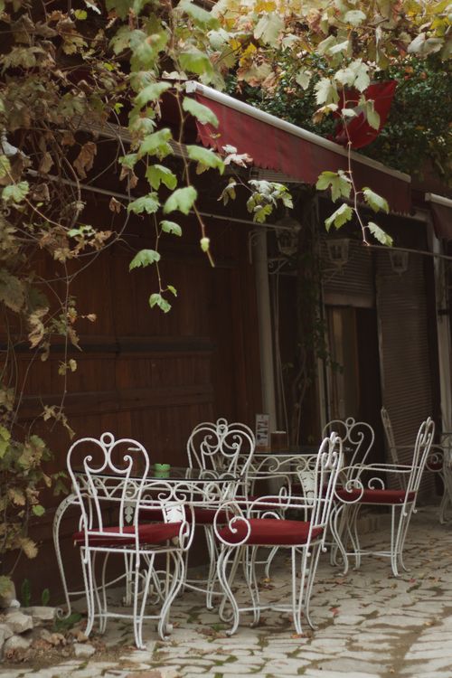 Free Cozy outdoor café setting with vintage iron chairs and lush foliage, perfect for summer relaxation. Stock Photo