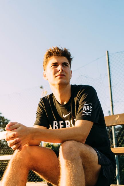 Young man sitting outdoors on a bench in sunlight, reflecting in a sports setting.