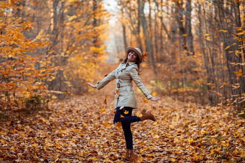 Free A woman joyfully poses among falling autumn leaves in a forest, embracing the vibrant fall season. Stock Photo