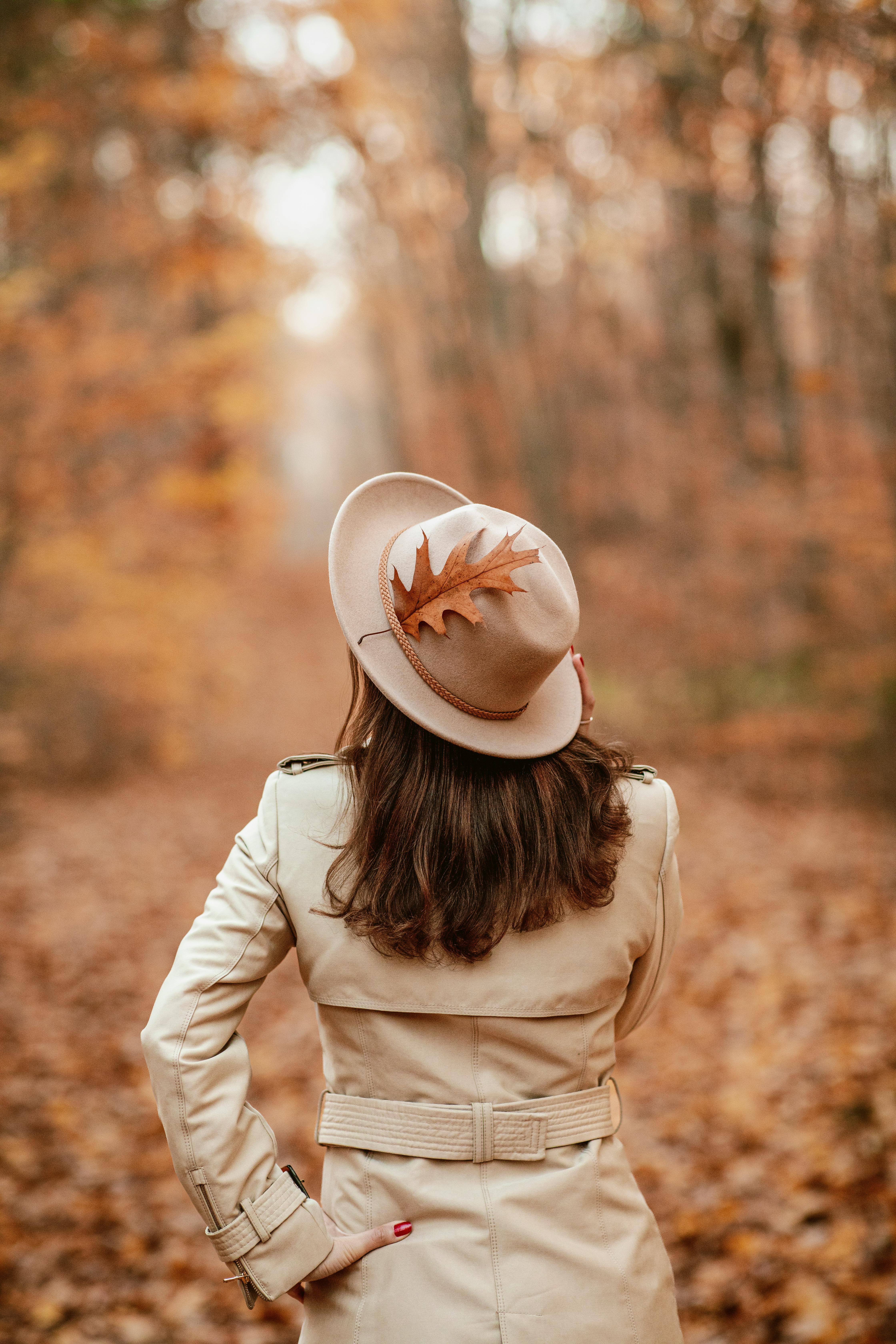 Back view of a woman in a coat and hat with a leaf, standing in an autumn forest.