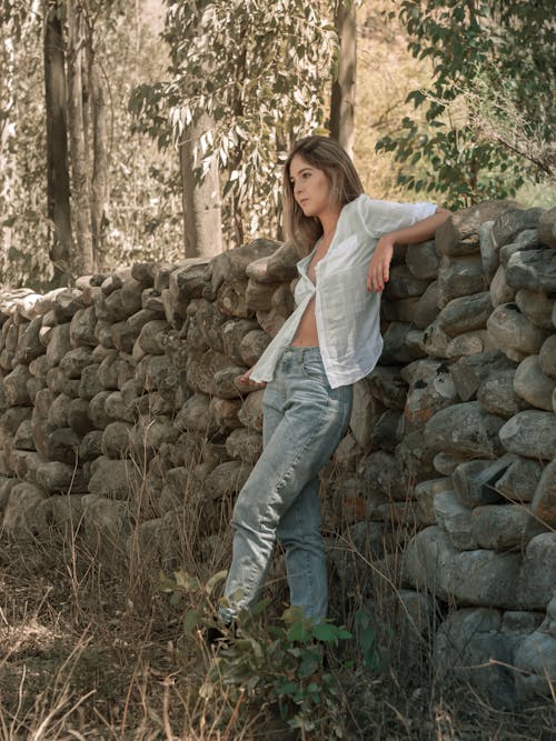 Beautiful Woman in White Shirt and Jeans Standing by Fence