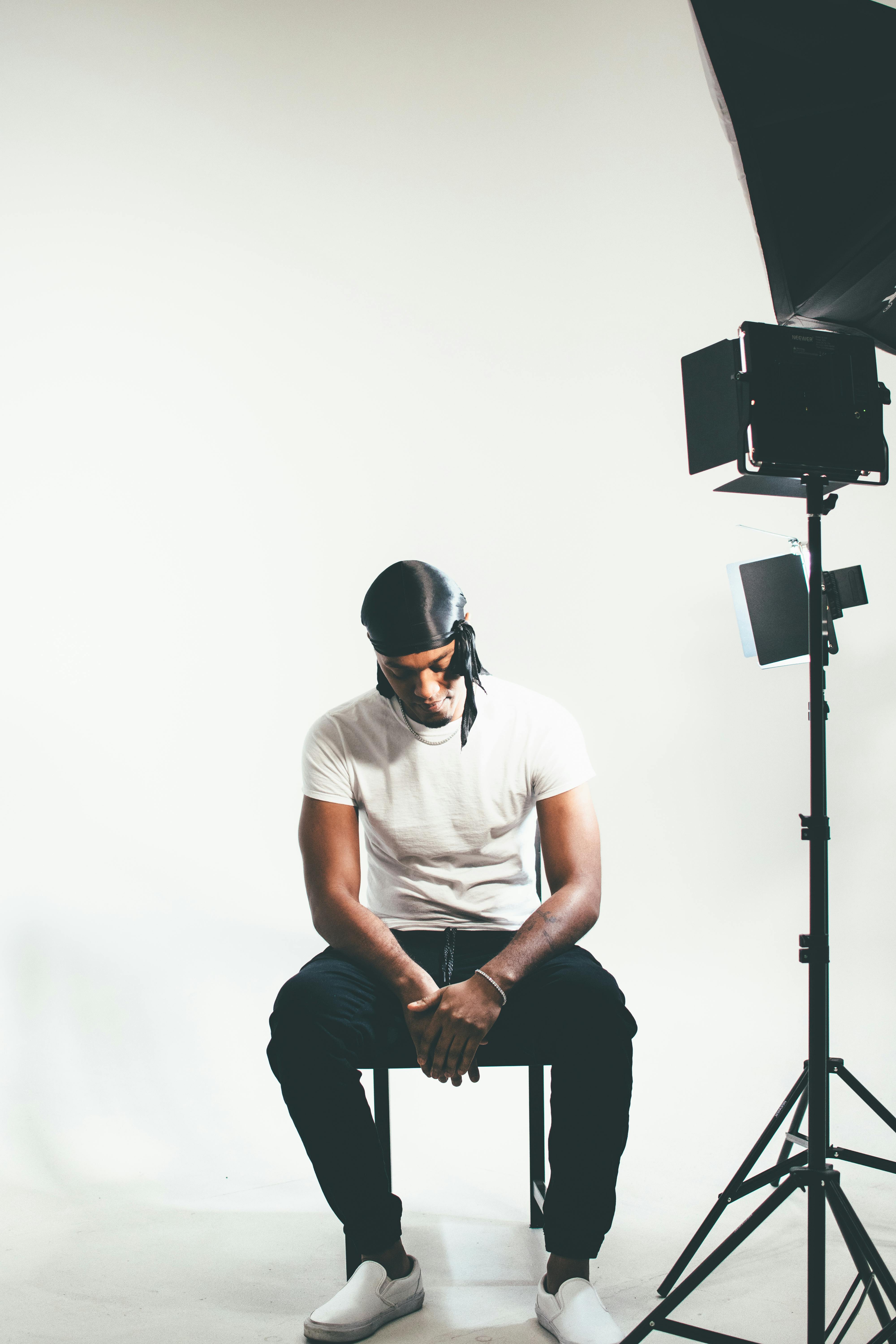 Stylish black male model seated in a minimalist studio with white background and studio lighting.