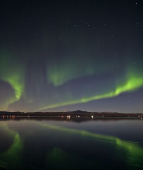 Stunning display of Northern Lights reflecting over a tranquil lake in Ölfus, Iceland at night.