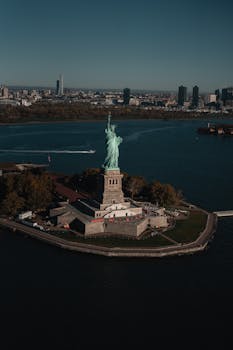 Drone shot of the iconic Statue of Liberty with Manhattan skyline in the background.
