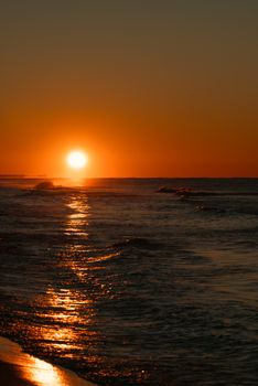 A serene ocean scene captured at sunset with vibrant orange hues reflecting on the water.