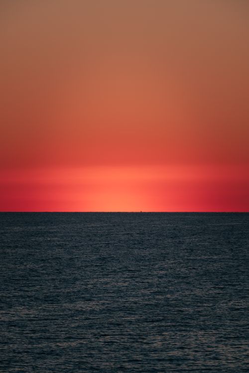 Free Stunning ocean sunset with vibrant red sky and peaceful waters, ideal for serene visuals. Stock Photo
