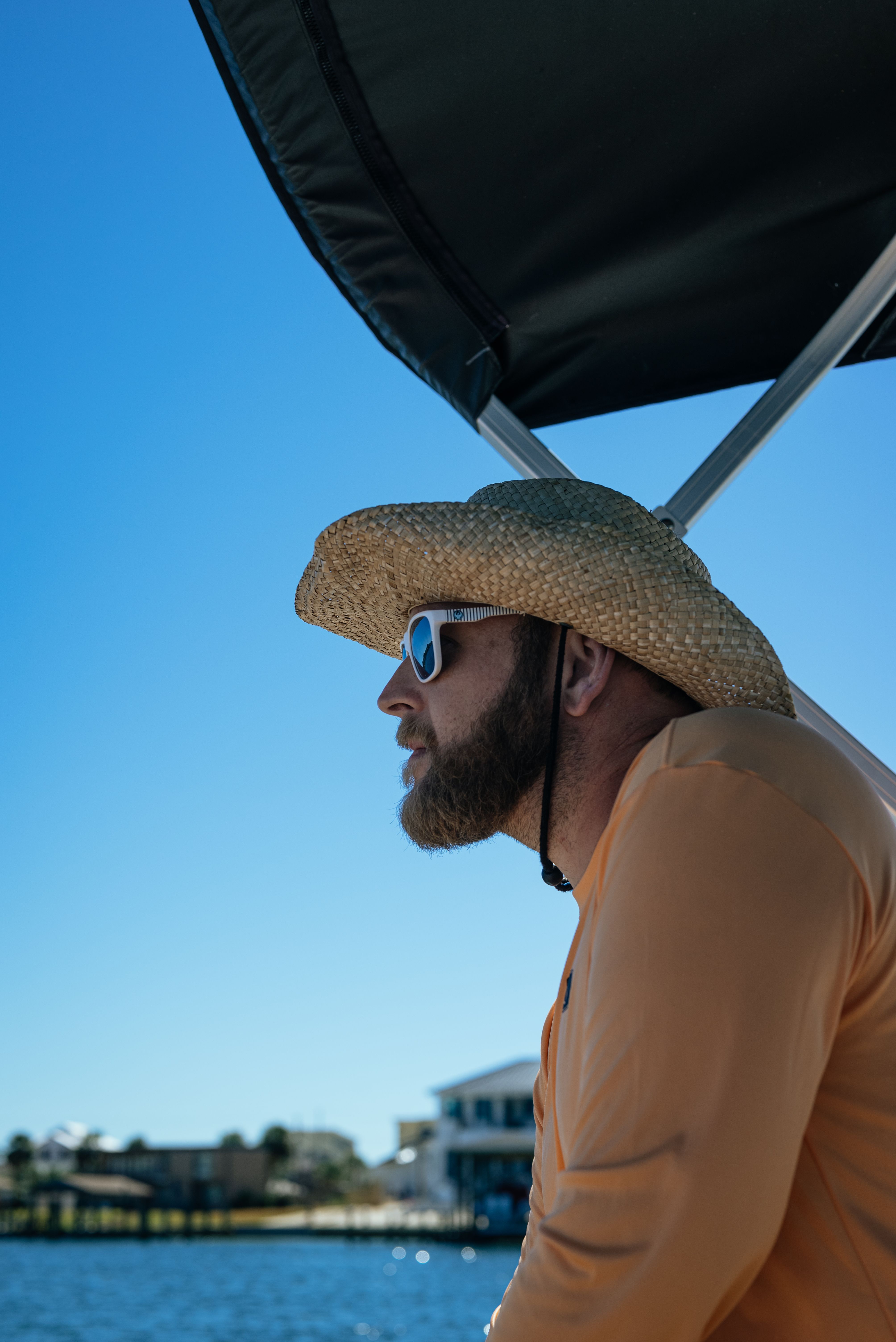 Bearded man in straw hat and sunglasses on boat under blue sky, enjoying summer leisure.