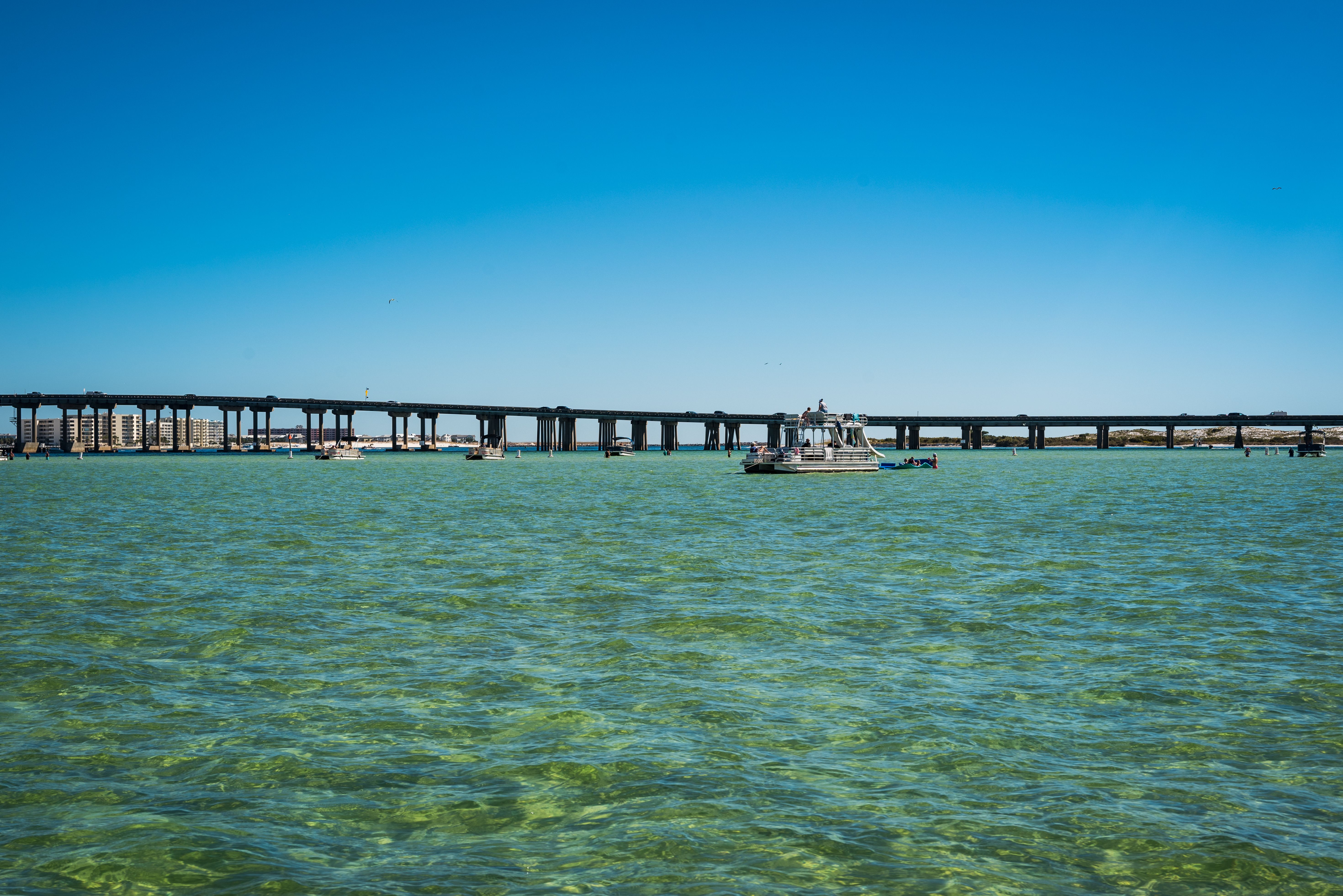 A scenic view of a bridge spanning across ocean waters with boats underneath on a sunny day.