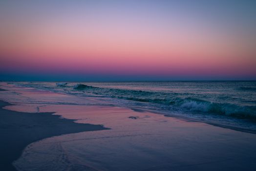 Calm ocean waves gently crash on the shore during a vibrant twilight sunset.