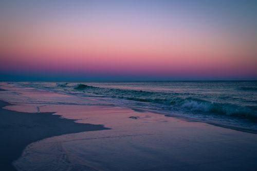 Free Calm ocean waves gently crash on the shore during a vibrant twilight sunset. Stock Photo