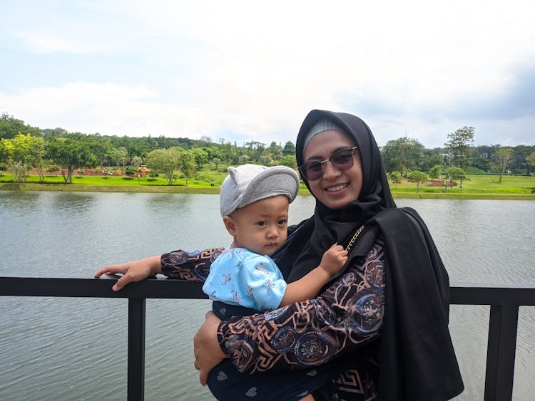 Woman In Black Hijab Wearing Sunglasses While Carrying Her Child