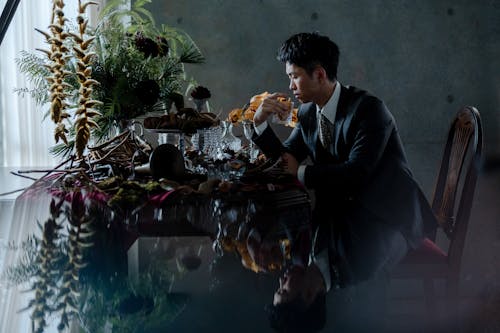 Man in Suit Sitting by Table with Flowers and Plants