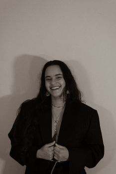 Studio portrait of a smiling woman in a black jacket, showcasing a stylish look with a chain necklace.