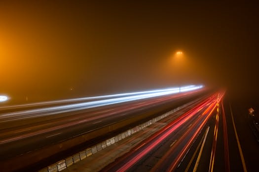 A dramatic long exposure shot of a foggy highway at night in Toronto, showcasing traffic lights and motion blur.
