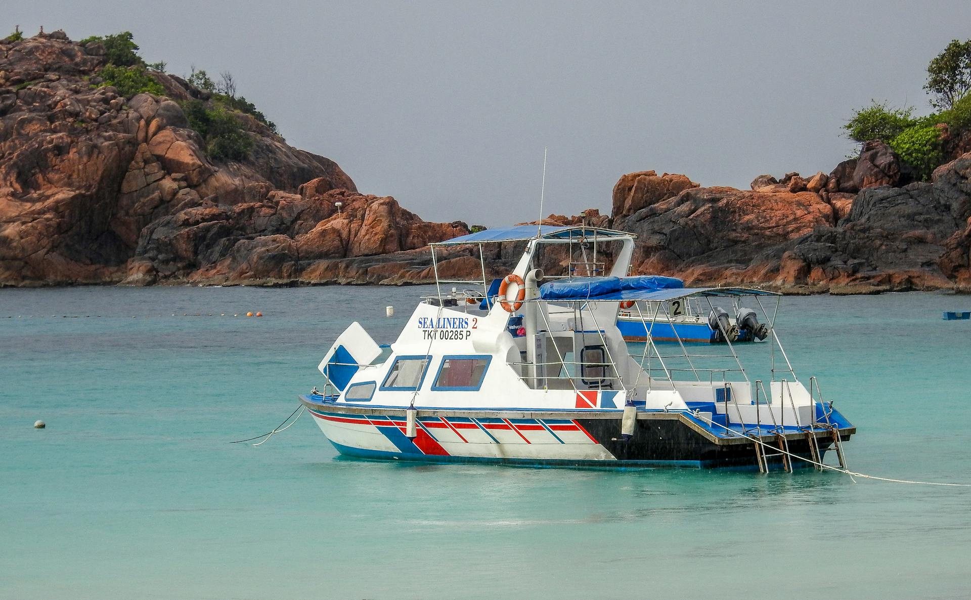 A vibrant boat anchored near rocky islands in a serene turquoise sea.