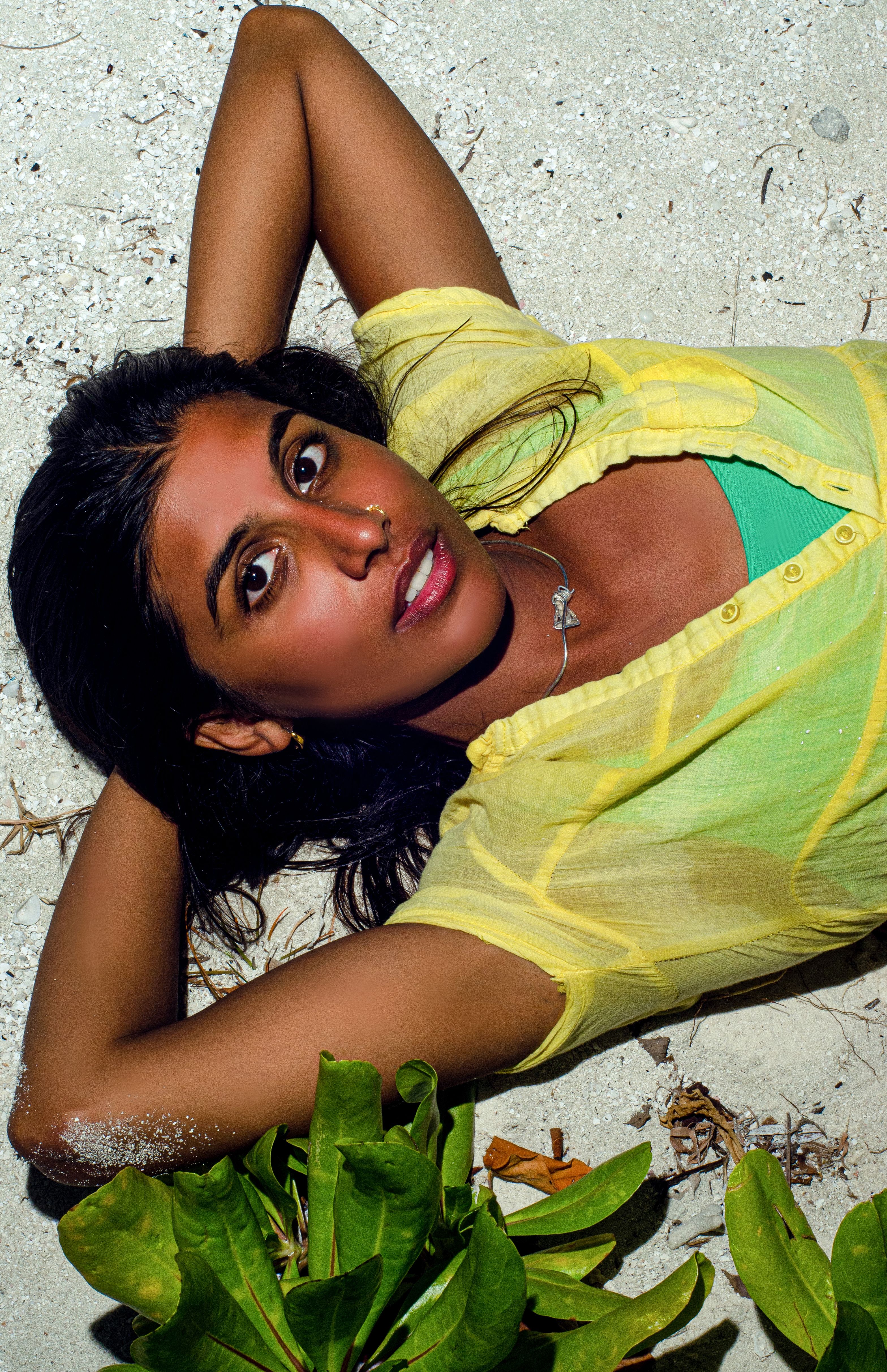 A woman in a yellow shirt enjoys a sunny day, lying on the beach sand.