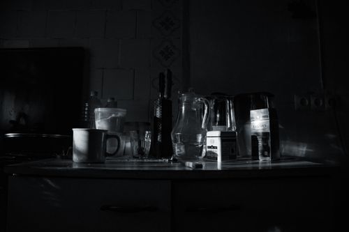 Free A moody kitchen scene featuring glassware, mugs, and containers in monochrome lighting. Stock Photo