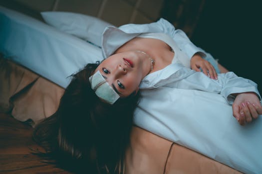 Close-up of a woman lying on a bed with a cooling pad on her forehead, indoors.