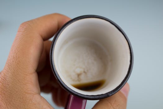 A close-up image of an empty coffee mug held in a hand, showing coffee residue.