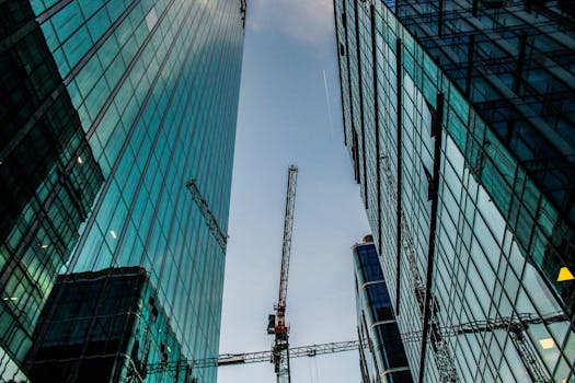 Looking up at modern skyscrapers with construction cranes in a bustling cityscape.