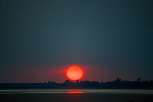 Dramatic sunset casting a warm glow over a serene landscape with calm waters.