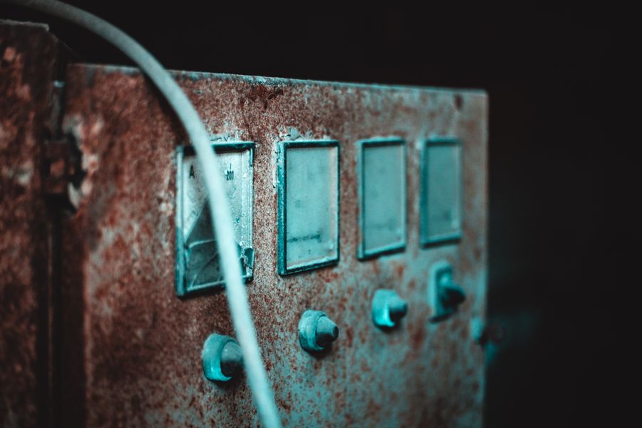 A close-up of an old, rusty electric panel with dials and a cable against a dark background.