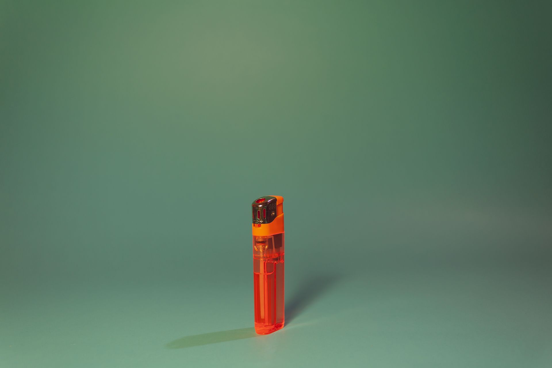 Simple orange lighter placed centrally on a smooth green background with minimalist style.