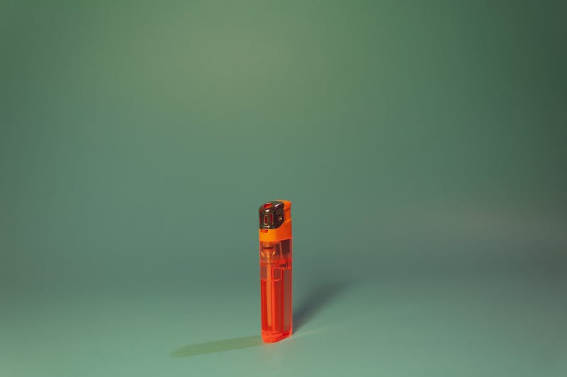 Simple orange lighter placed centrally on a smooth green background with minimalist style.