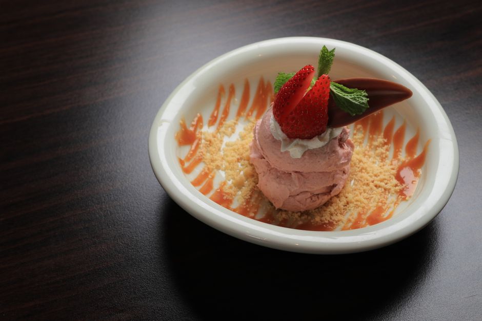 A scoop of pink-streaked strawberry shortcake ice cream in a bowl, studded with golden shortbread crumbs and a few fresh strawberry slices on top.
