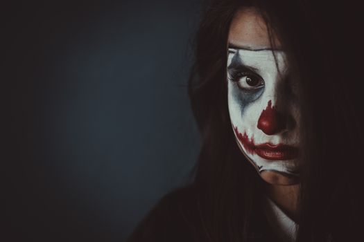 Moody portrait of a woman with clown face paint, exemplifying creative makeup and Halloween themes.