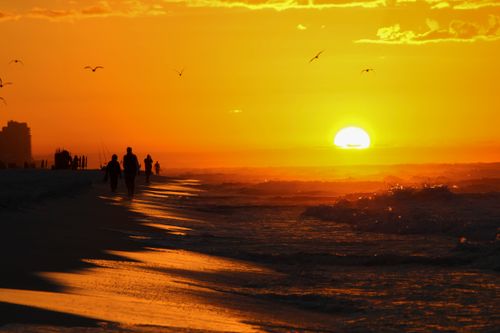 Free Silhouetted figures walking along a beach at sunset, capturing a serene and vibrant scene. Stock Photo