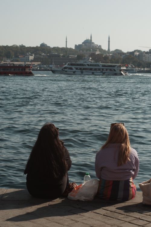 Free Two women sitting by the water, enjoying views of boats and the Istanbul skyline. Stock Photo