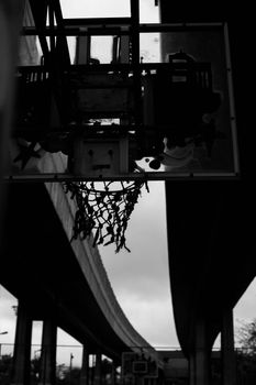 Silhouette of a basketball hoop below an overpass, captured in grayscale.
