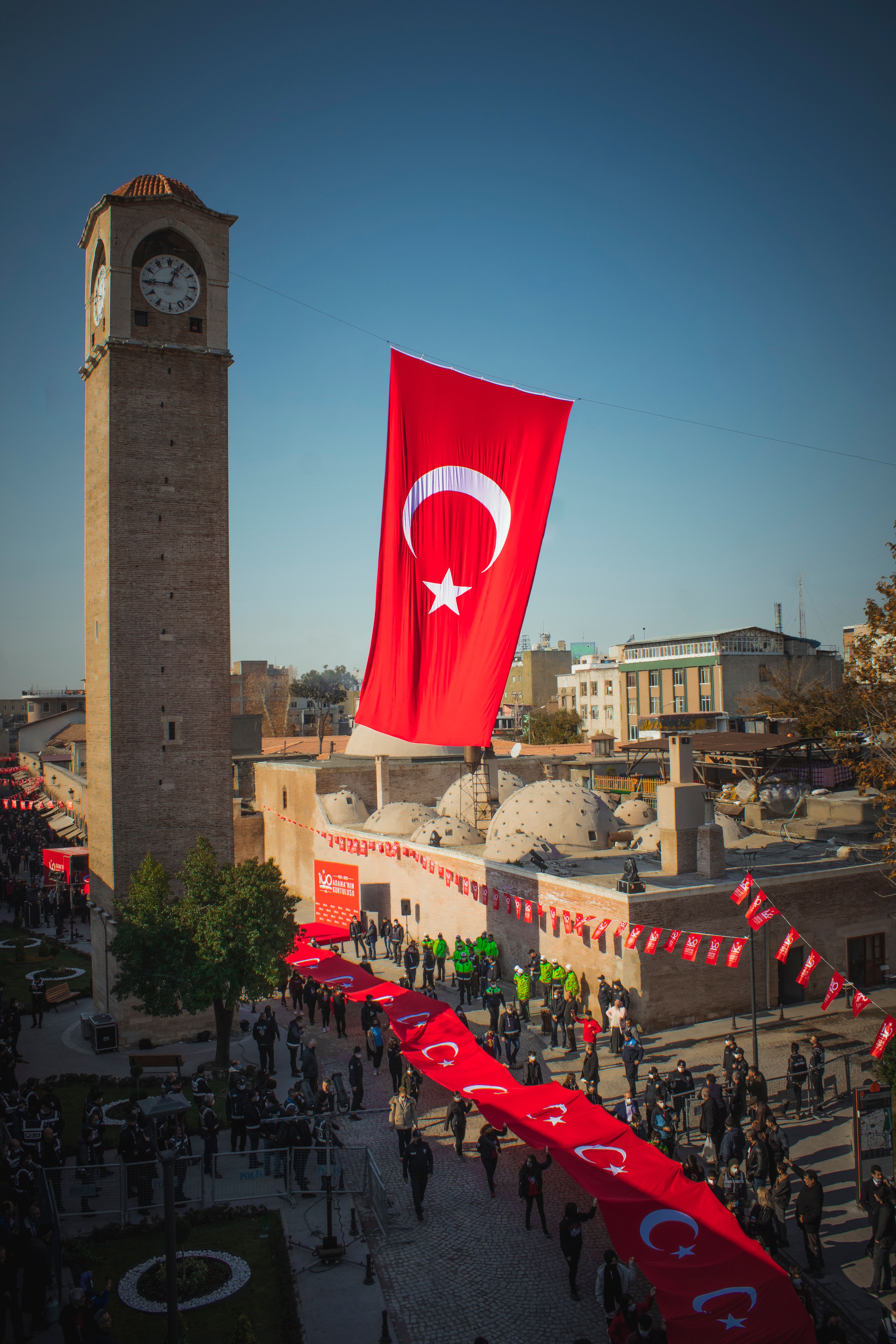 View of a Turkish flag and clock tower in Adana, capturing a vibrant street scene with cultural elements.