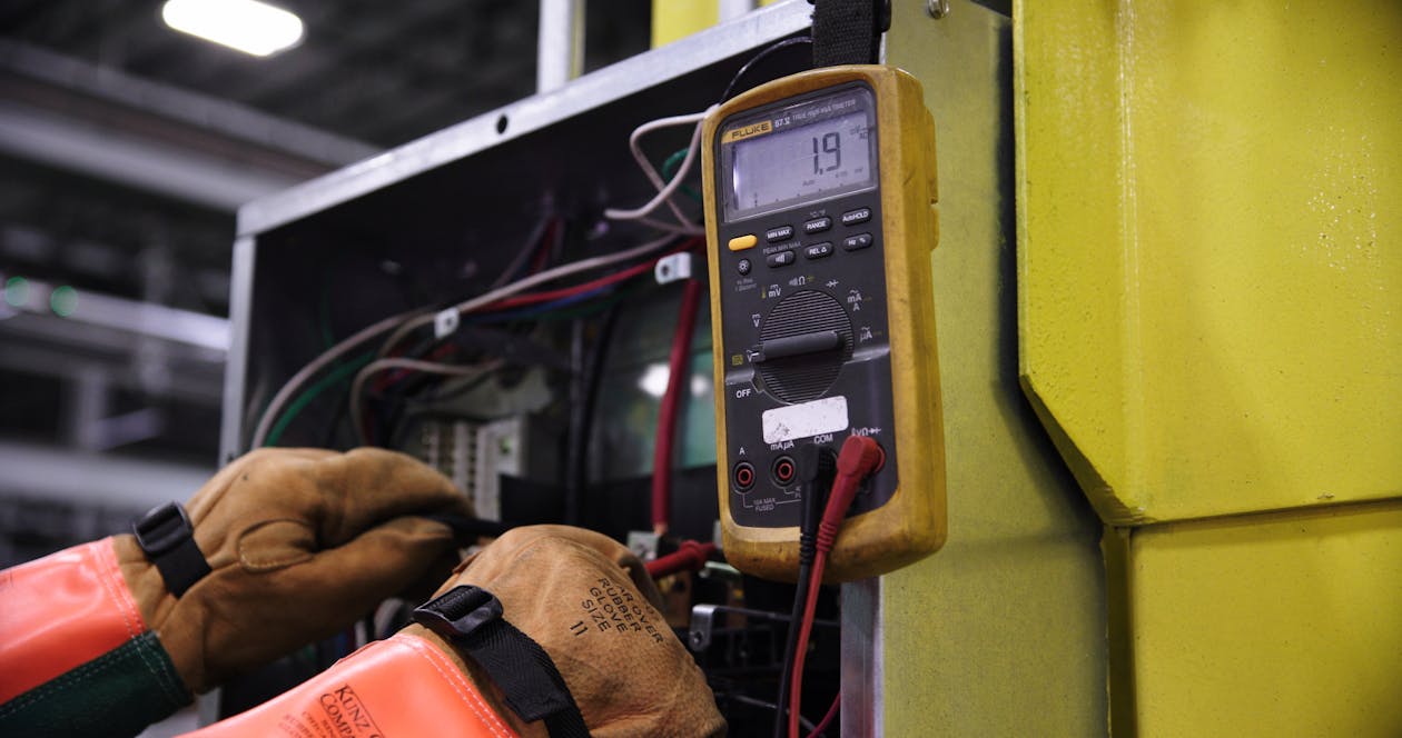Free Electrician using a multimeter to fix industrial control panel wiring. Stock Photo