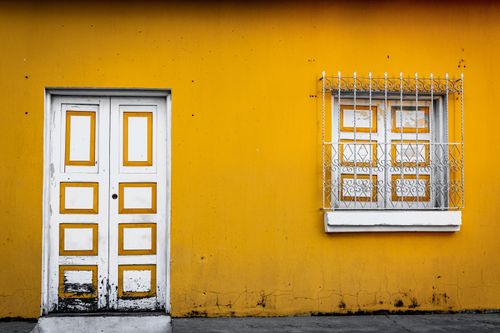 Free A striking yellow wall featuring a classic white door and window with intricate metalwork. Stock Photo