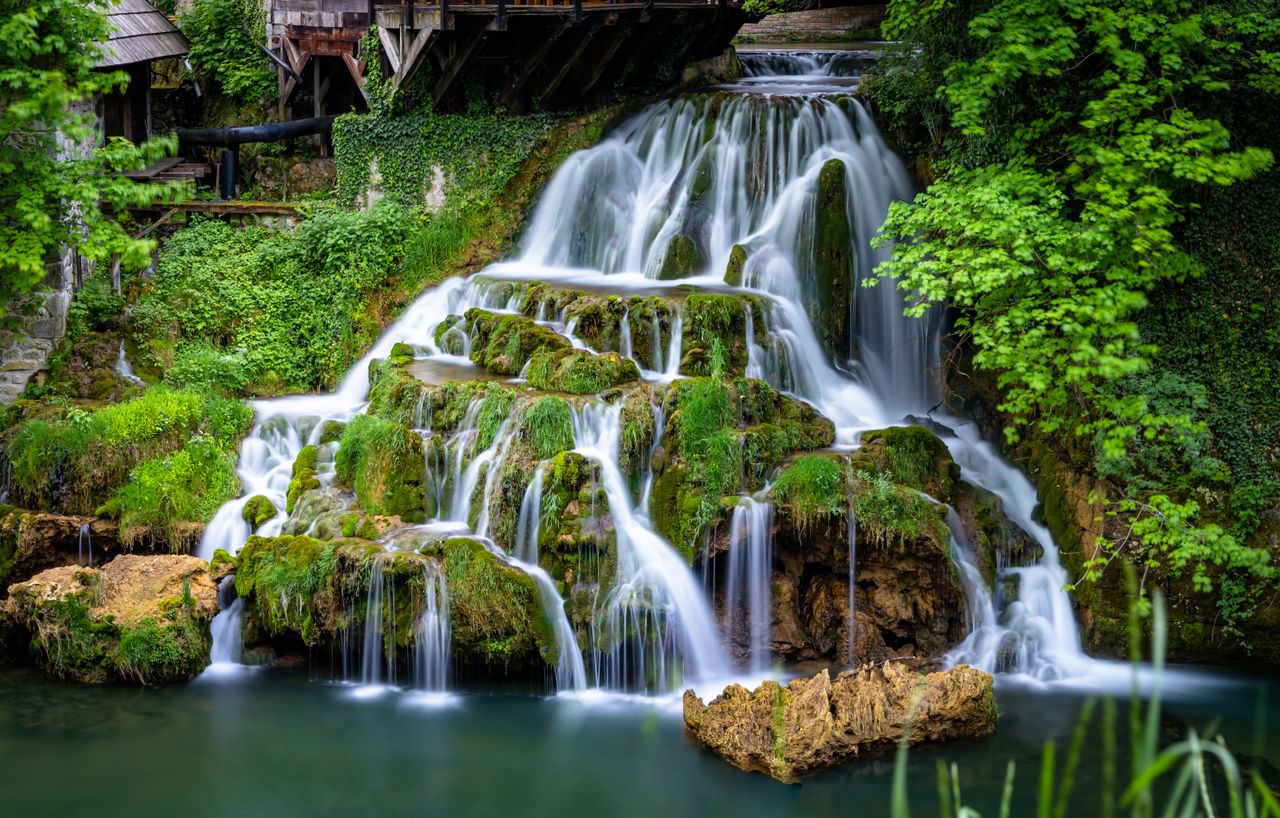 scenic waterfall cascading over mossy rocks surrounded by lush greener