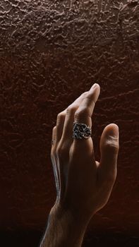 Close-up of hand with silver rings against textured brown background.