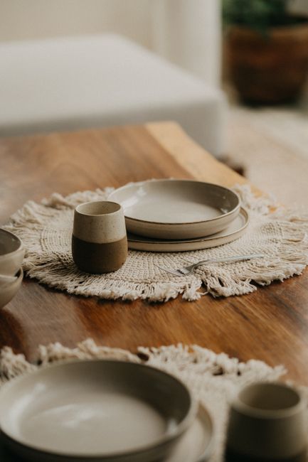Stylishly arranged ceramic plates and cups on a wooden table with woven placemats, embodying rustic elegance.