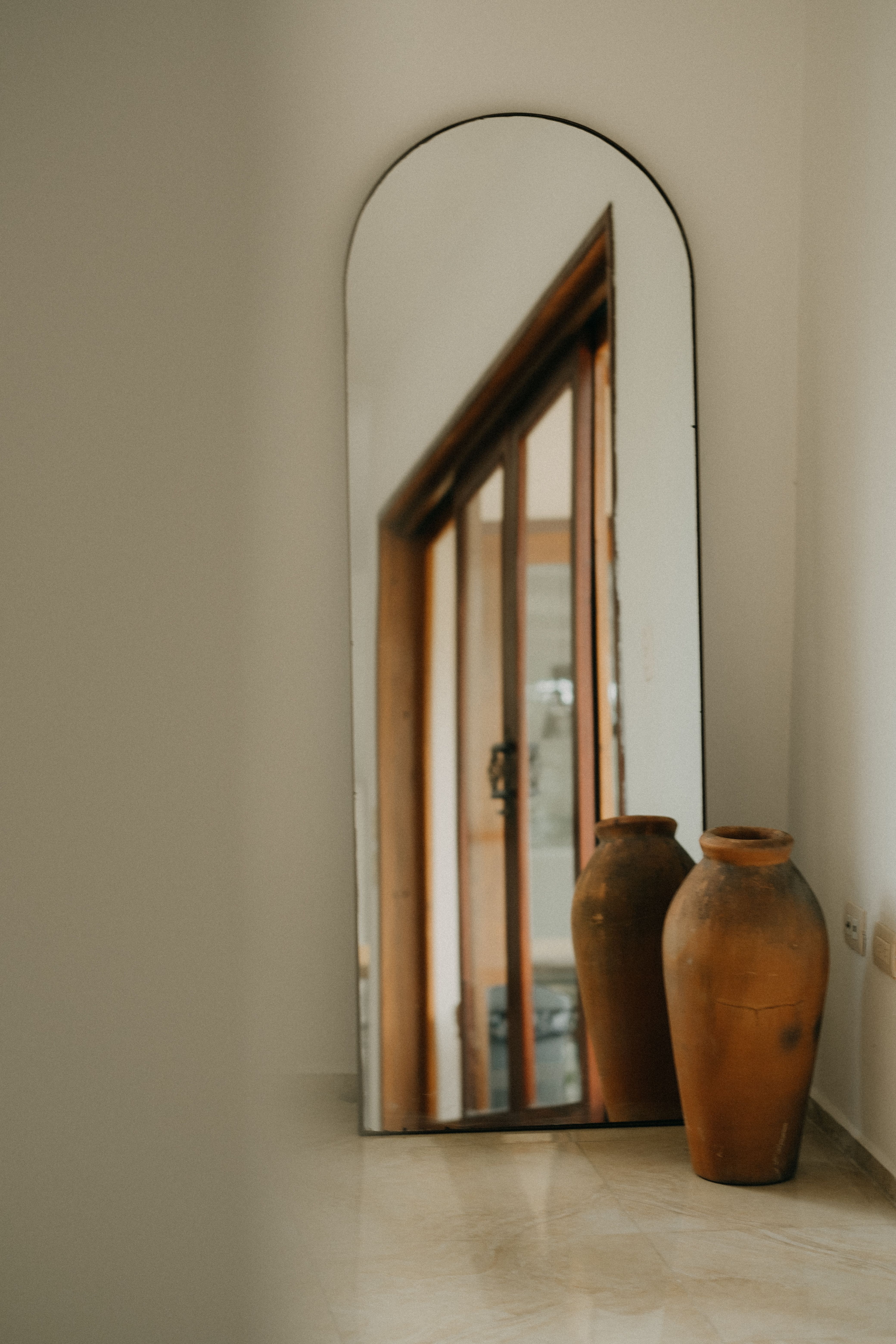 Sophisticated interior featuring a large arched mirror with terracotta vases for a warm decor style.