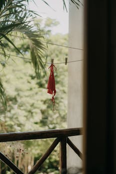 A red bikini top drying on an outdoor clothesline with lush greenery in the background.
