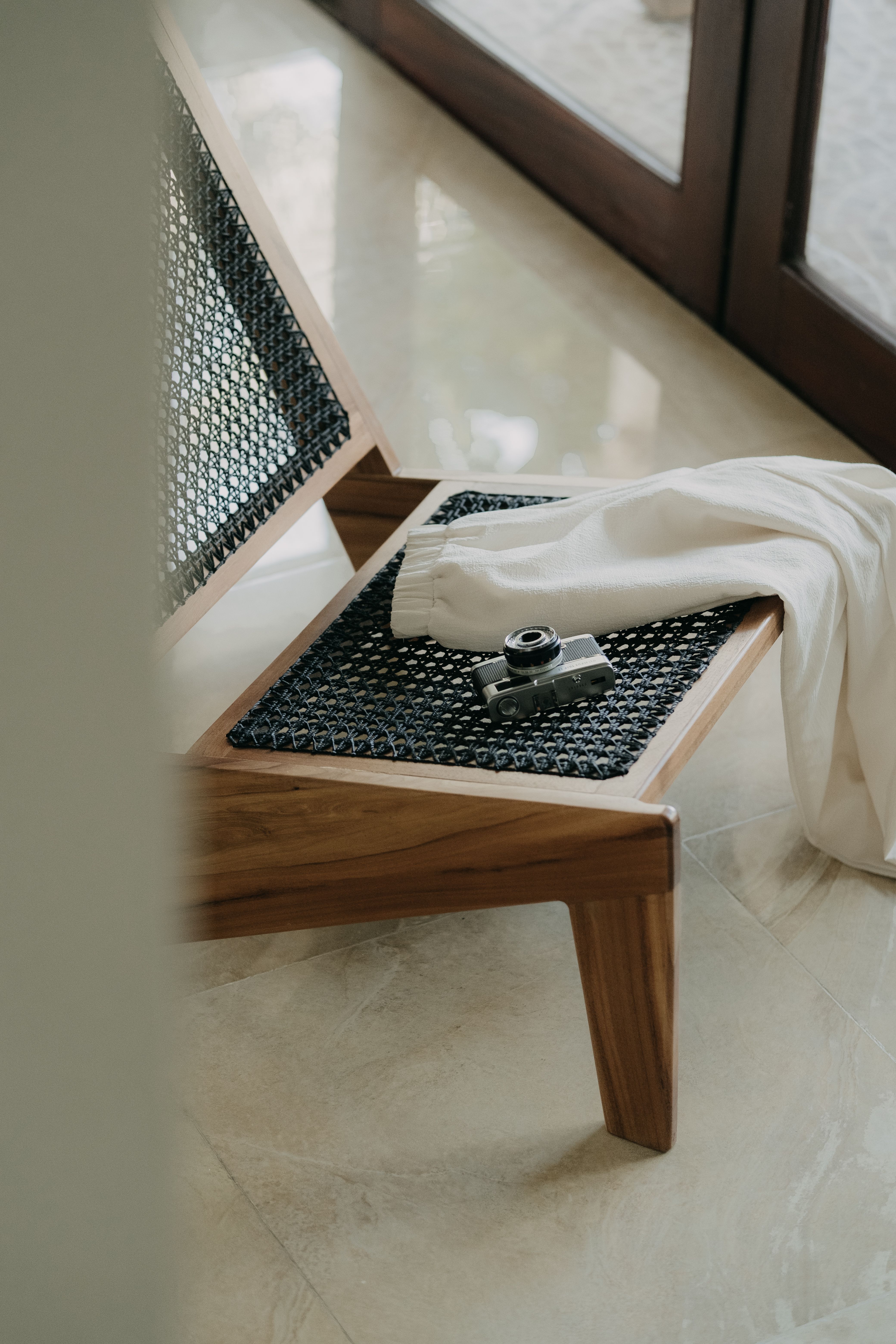 A vintage camera rests on a wooden chair, accompanied by white pants, set in an indoor setting.