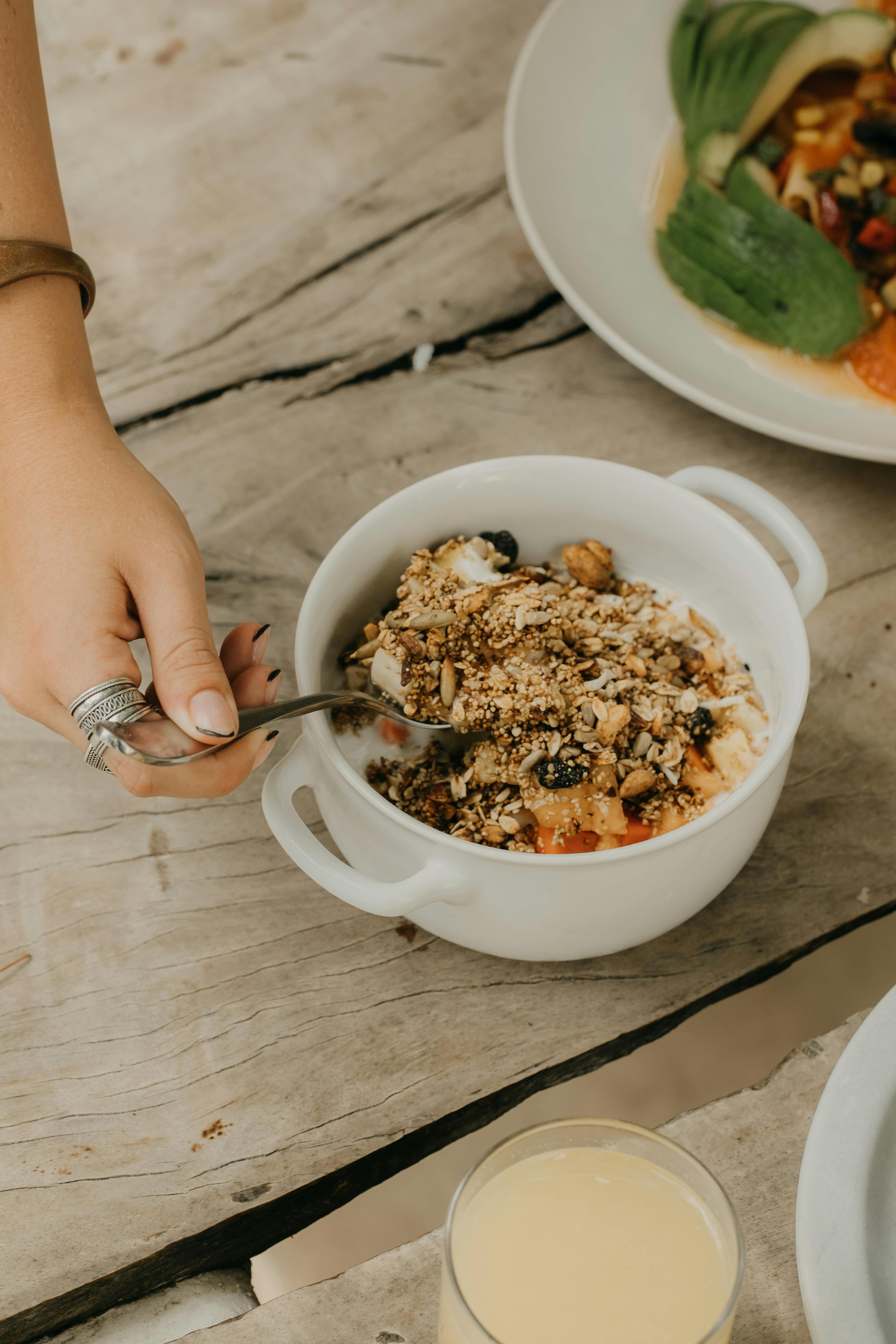 A hand scooping delicious granola from a healthy breakfast bowl on a rustic wooden table.