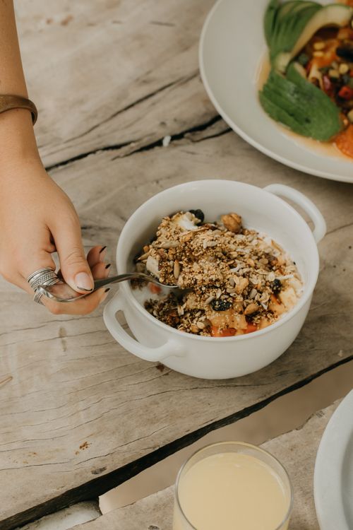 Free A hand scooping delicious granola from a healthy breakfast bowl on a rustic wooden table. Stock Photo