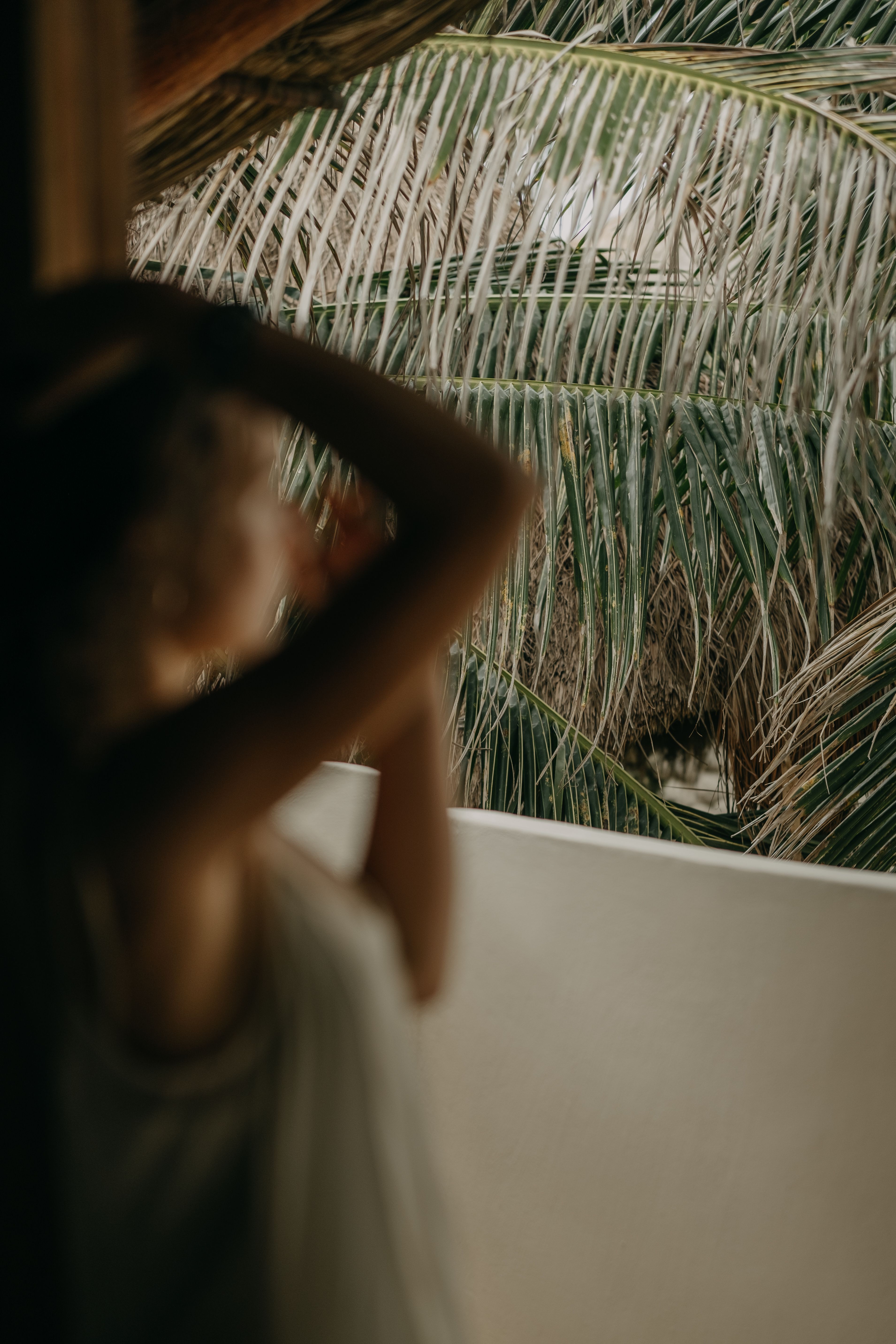 A serene moment with a blurred woman on a balcony, framed by palm leaves.