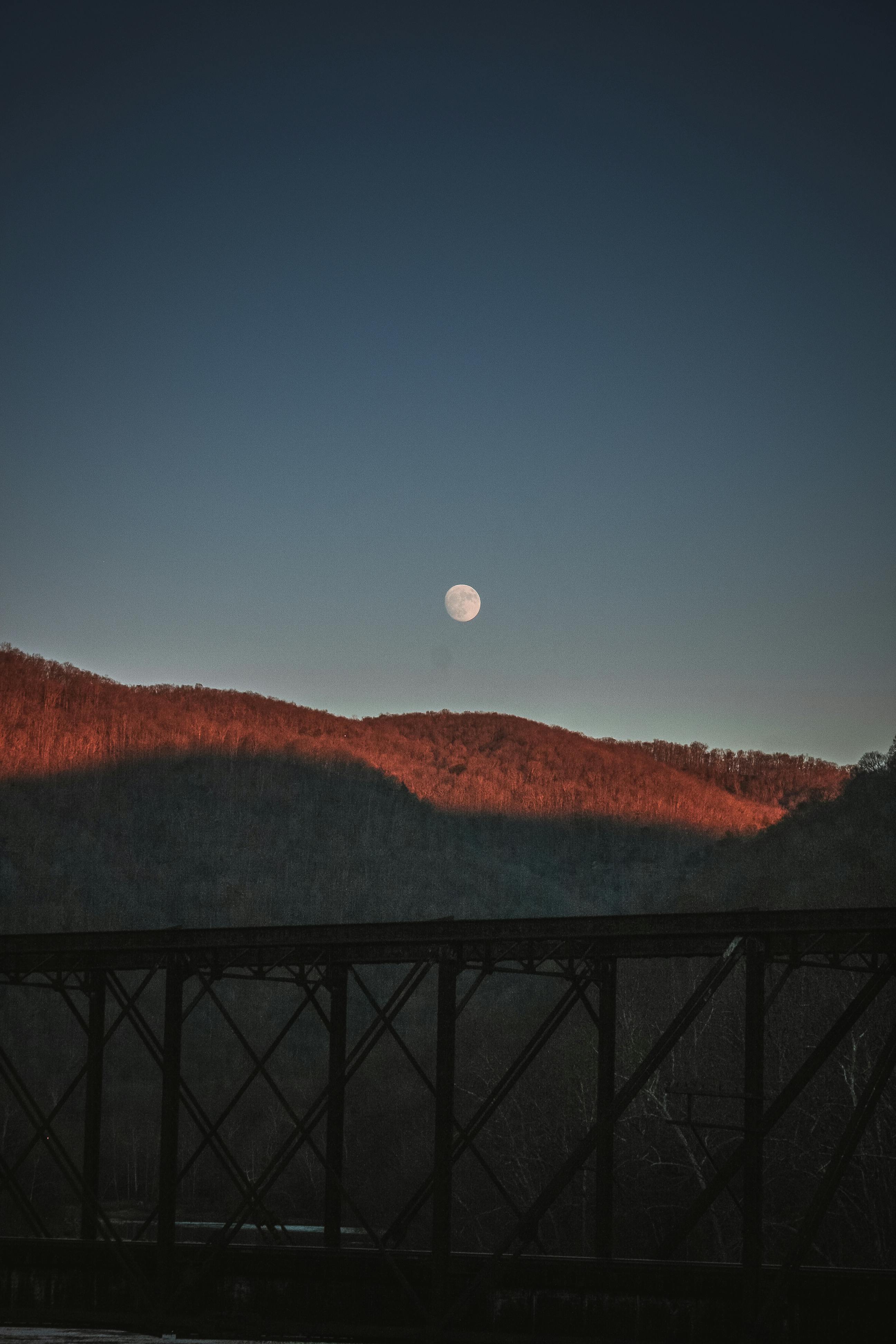 日落时分，山脉的美丽轮廓前，满月与桥梁构成了前景