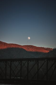 日落时分，山脉的美丽轮廓前，满月与桥梁构成了前景