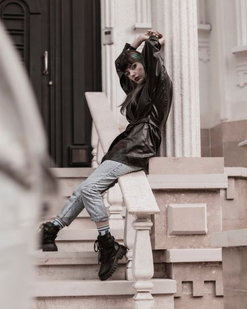 Free Young stylish woman in a black leather jacket poses on stairs in an urban setting, exuding confidence. Stock Photo