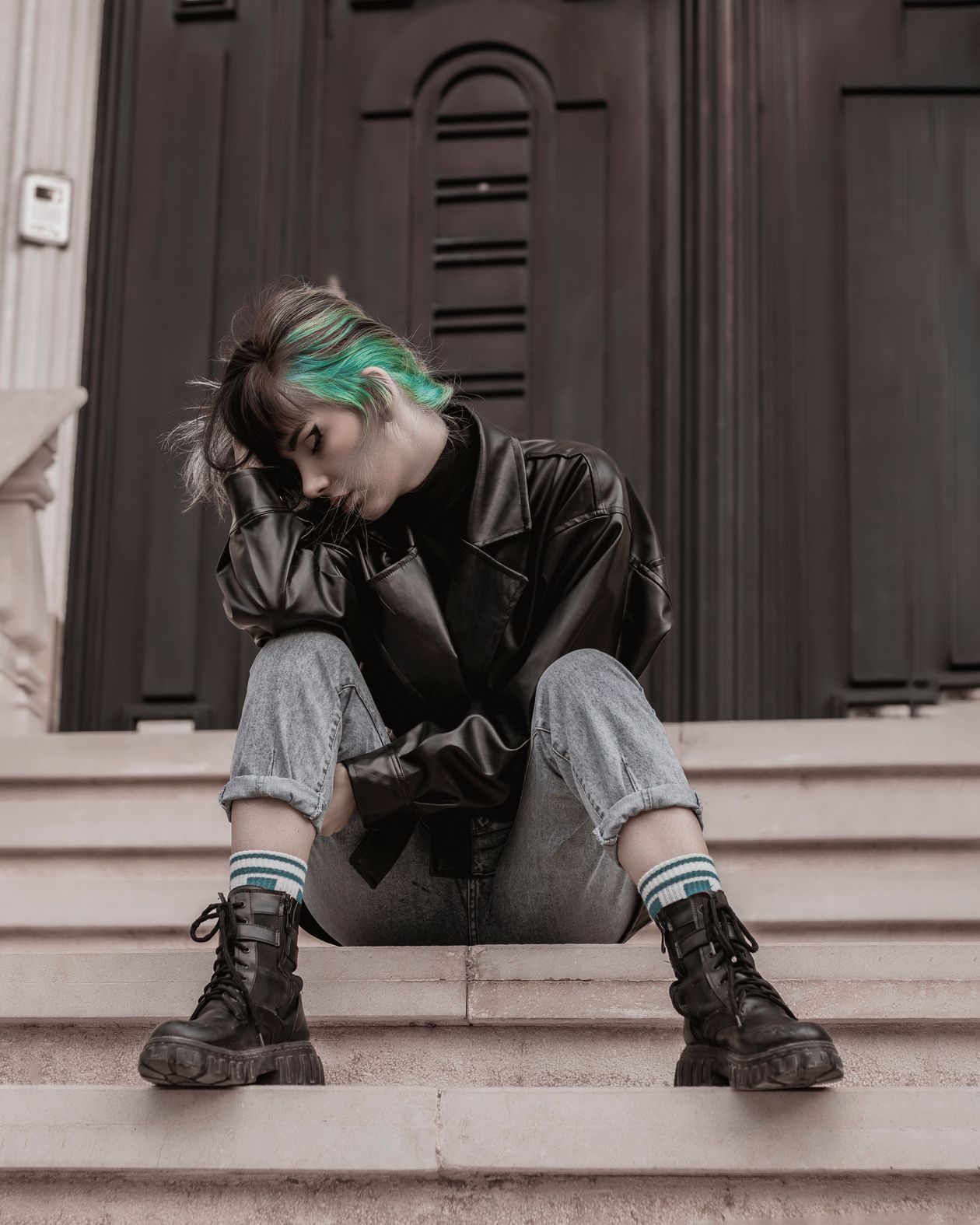 Woman with green-tinted hair wearing a black leather jacket, cuffed jeans and chunky black lace-up boots
